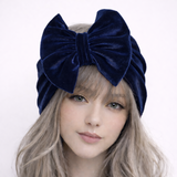 Woman wearing a navy blue velvet headband with a large bow on a white background