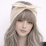 Woman with long, wavy hair wearing a beige headband against a white background