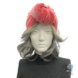 Mannequin head with gray hair wearing a pink velvet turban on a white background