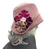 A dusty pink fabric bucket hat with a large decorative floral embellishment, shown on a mannequin head with gray hair against a plain white background.