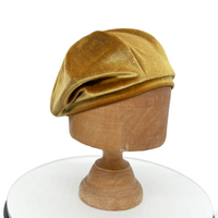 Gold velvet beret on a wooden mannequin head against a white background