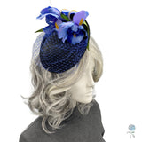 May include: A blue and black fascinator with a blue veil and blue and yellow flower accents.