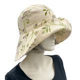 May include: A wide-brimmed sun hat with a floral embroidery design in shades of green, purple, and blue. The hat is made of a light beige fabric.