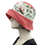 Eleanor cloche hat with a wide front brim for women handmade in dusky coral linen and a floral cotton accent band finished with a coral green and white peony flower brooch side view