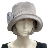 Handmade Gray Linen 1920s Style cloche hat with wide front brim and chiffon flower brooch. Modeled on a mannequin head. Front view showing the brooch. Boston Millinery