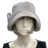 Handmade Gray Linen 1920s Style cloche hat with wide front brim and chiffon flower brooch. Modeled on a mannequin head. Front view showing the brooch. Boston Millinery