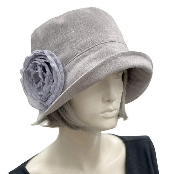 Handmade Gray Linen 1920s Style cloche hat with wide front brim and chiffon flower brooch. Modeled on a mannequin head. Front side view showing the brooch. Boston Millinery